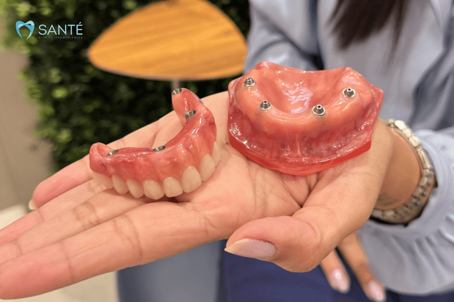 Mão segurando uma dentadura móvel superior, exemplificando a falta de fixação que causa insegurança ao falar e comer.